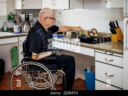 Ein Mann mit zwei Gliedmaßen, der auf dem Herd in der Küche zu Hause kocht Albert, Alberta, Kanada Stockfoto