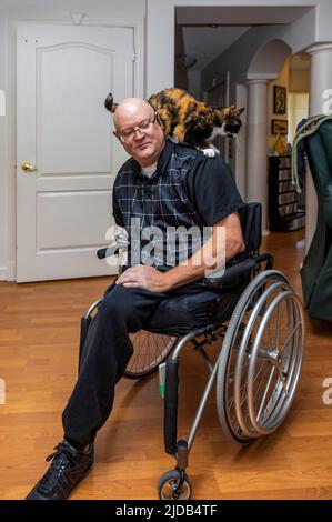 Ein Mann mit zwei Gliedmaßenamputationen, der in seinem Haus saß und seine Katze über seine Schultern krabbelte Albert, Alberta, Kanada Stockfoto