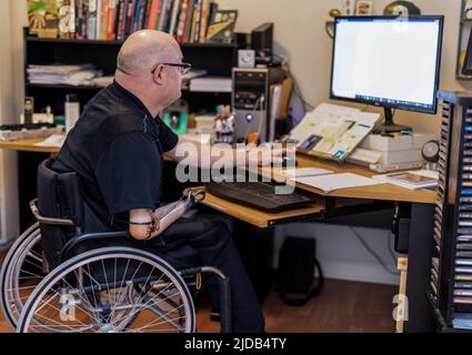 Ein Mann mit einer Amputation von zwei Gliedmaßen, der von zu Hause aus an einem Computer arbeitet Albert, Alberta, Kanada Stockfoto