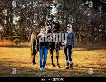 Ein junges Mädchen mit Zerebralparese posiert mit ihrer Mutter, ihrem Trainer und einem Pferd während einer Hippotherapie-Sitzung nach einem Trail-Ritt Stockfoto