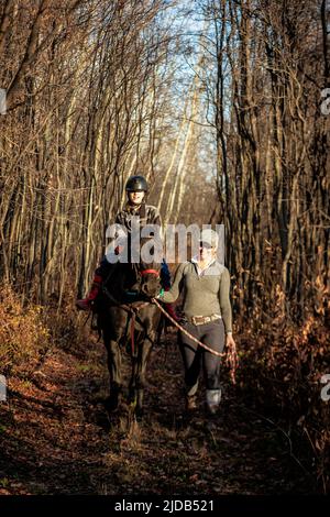 Ein junges Mädchen mit Zerebralparese und ihr Trainer, der mit einem Pferd während einer Hippotherapie auf einem Trail-Ritt arbeitet; Westlock, Alberta, Kanada Stockfoto