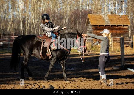 Ein Trainer, der mit einem jungen Mädchen mit Zerebralparese während einer Hippotherapiesitzung arbeitet; Westlock, Alberta, Kanada Stockfoto