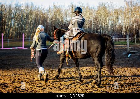 Ein Trainer, der mit einem jungen Mädchen mit Zerebralparese während einer Hippotherapiesitzung arbeitet; Westlock, Alberta, Kanada Stockfoto