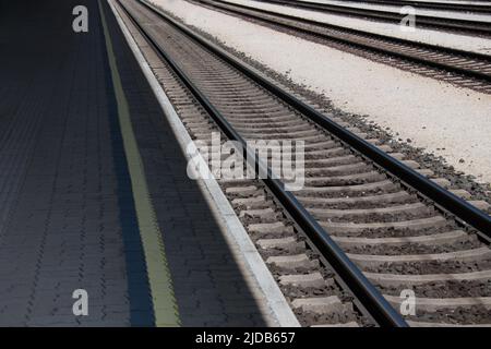 Nahaufnahme Teilansicht einer mit Betonblöcken gepflasterten Plattform neben einer Stahleisenbahn, die diagonal durch das Bild als Konzept für tra führt Stockfoto