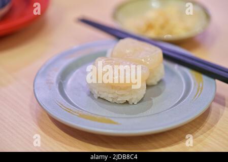 Nahaufnahme von rohem Jakobsmuscheln-Sushi in einem Gericht auf einem Restauranttisch. Gesunde Meeresfrüchte Mahlzeit mit japanischem Essen. Stockfoto