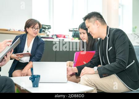 Ein lächelnder Geschäftsmann diskutiert und zeigt einer jüngeren Kollegin etwas im Laptop. Mentoring oder Training am Arbeitsplatz. Stockfoto