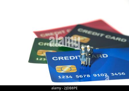 Miniatur Menschen Spielzeug konzeptuelle Fotografie. Ein älteres Paar, das über der Kreditkarte steht, bezahlt und Haushaltsgegenstände kauft. Bildfoto Stockfoto