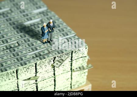 Miniatur Menschen Spielzeug konzeptuelle Fotografie. Ein älteres Paar, das über dem Geldstapel steht. Finanz- und Sparkonzept. Bildfoto Stockfoto