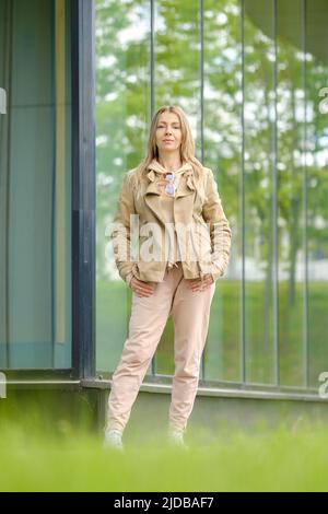 Die sportliche Frau im Anzug steht in der Nähe der verstärkten Glaswand ihrer Wohnung Stockfoto