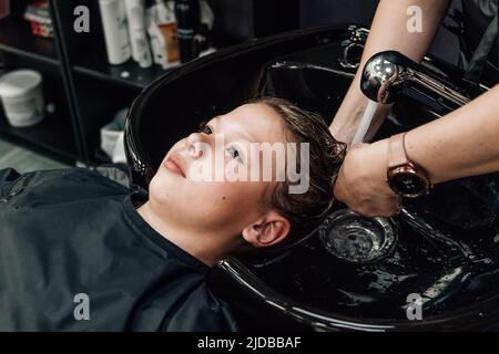 In einer Elite-Friseurin wäscht die schöne junge Frau ihren Kopf in einem speziellen Stuhl. Das Konzept, den Kopf in einem Schönheitssalon zu waschen Stockfoto