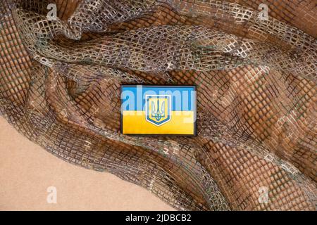 Patch auf der militärischen Uniform Flagge der Ukraine gelb-blau liegt auf einem grünen Tarnhintergrund, militärischen Hintergrund, die Armee der Ukraine Stockfoto