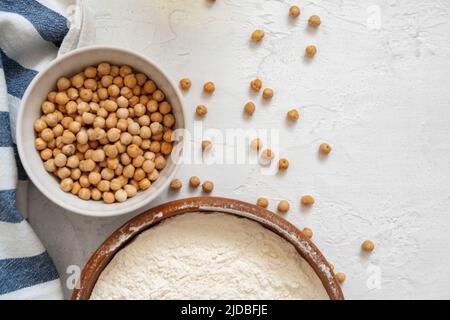 Kichererbsen und Mehl in Keramikschale auf weißem Hintergrund Stockfoto
