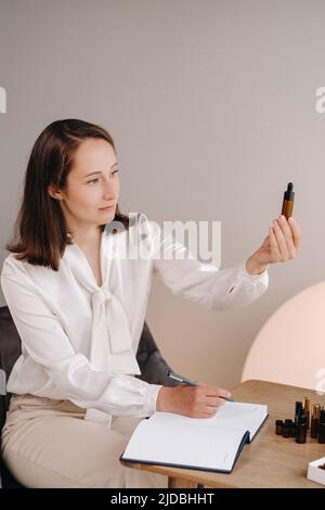 Das Aromatherapeutin-Mädchen sitzt in ihrem Büro und hält eine Flasche aromatisches Öl in den Händen und schreibt etwas auf. Es gibt ätherisches Öl Stockfoto