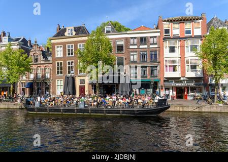 Leiden, Niederlande - 6. Mai 2022: Bootsterrasse voller Leute, die die Sonne, Essen und Getränke genießen. Das Café im Freien ist eine wichtige Freizeitbeschäftigung Stockfoto