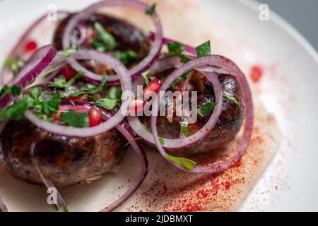 georgische gebratene Schweinefleischwürste kupaty mit Zwiebeln, Koriander auf Pita auf weißem Teller Stockfoto