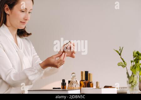 Das Aromatherapeutin-Mädchen sitzt in ihrem Büro und hält eine Flasche aromatischer Öle. Auf dem Tisch liegen ätherische Öle. Stockfoto