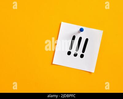 Drei handgeschriebene Ausrufezeichen auf einem Notizpapier, das an einem gelben Brett befestigt ist. Wichtiges Hinweiskonzept. Stockfoto