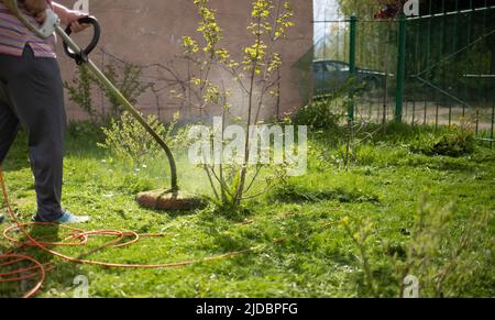 Ältere Frau mäht das Gras mit einem Trimmer Stockfoto