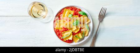 Ravioli mit Tomatensauce und Basilikum mit einem Glas Weißwein, ein Panorama für ein italienisches Restaurant-Menü, über dem Kopf flach liegend Stockfoto