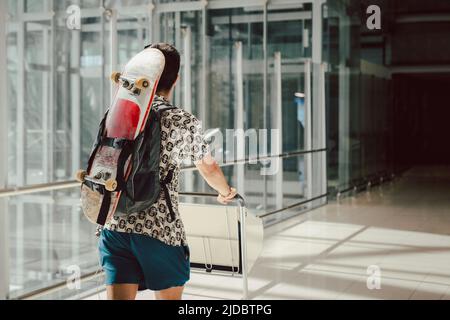 Junger Mann, der am Flughafen mit Skateboard auf dem Rücken läuft. Stockfoto