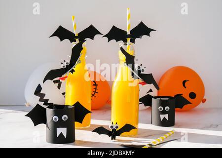 Halloween-Mocktails. Oranger alkoholfreier Cocktail für Halloween-Party auf weißem Tisch. Die Trinkhalme sind mit geschnittenen Papierfledermäusen verziert. Halloweens gruseliges dri Stockfoto