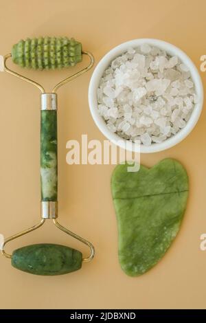 Gesichtswalzen Gouache Massagegerät Scraper, aus natürlichem Amethyst. Selbstpflege-Set. Home Spa-Produkte auf neutralem beigen Hintergrund. Gesichtsbehandlungen Stockfoto