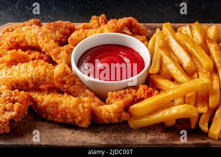 Hähnchenbrötchen, paniert und gebraten, mit einem roten Dip und Pommes frites, eine Nahaufnahme auf Schwarz Stockfoto