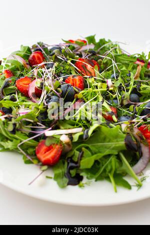 Leichter Salat mit Rucola und Beeren, Erdbeeren und Blaubeeren, köstlicher gesunder Sommersalat auf weißem Hintergrund Stockfoto