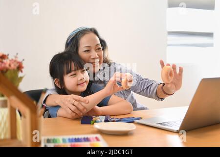 Liebevolle reife Oma und kleine Enkelin, die zu Hause einen Videoanruf auf einem Laptop-Computer haben. Multi-Generationen-, Familien- und Liebeskonzept Stockfoto