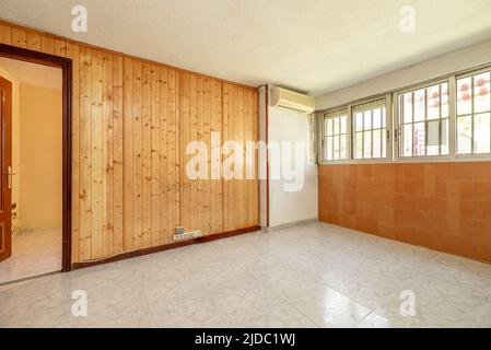 Leeres Zimmer mit Wänden, die mit Kiefernnut bedeckt sind, Fenstern an einer Wand und Klimaanlage Stockfoto