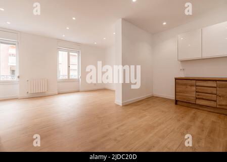 Leeres Wohnzimmer mit offener Küche mit Kastanienholzmöbeln, Holzböden und schlichten weiß gestrichenen Wänden Stockfoto