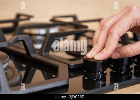 Weibliche Hand, die die Temperatur auf dem Bedienfeld des Gaskochfelds anpasst, Frau, die einen Gasherd verwendet, moderne Haushaltsgeräte Stockfoto