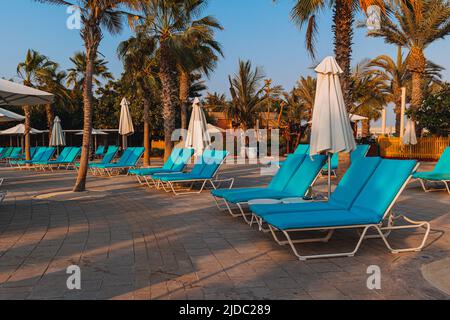 Blue-Bett-Pool mit einem Handtuch stehen unter Sonnenschirmen vor dem Hintergrund der schönen Palmen, Ruhe, Urlaub, Entspannung. Stockfoto