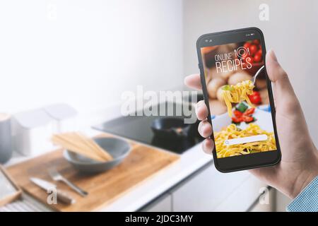 Frau, die in ihrer Küche eine Mahlzeit zubereitet, sucht mit ihrem Smartphone POV shot in einer Koch-App nach gesunden Rezepten Stockfoto