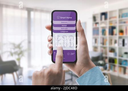 Frau mit einer Smart Home Automation App auf dem Smartphone, Rauminnenraum im Hintergrund Stockfoto