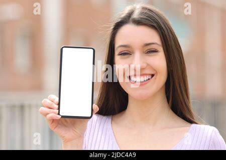 Vorderansicht Porträt eines glücklichen Teenagers, der auf der Straße einen leeren Bildschirm des Smartphones zeigt Stockfoto