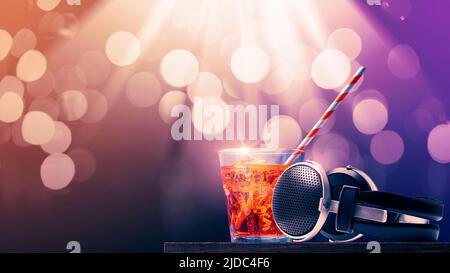 Köstlicher Cocktail und Kopfhörer auf einem Tisch im Tanzclub, Bokeh-Disco-Lichter im Hintergrund, Kopierraum Stockfoto