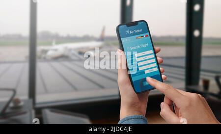 Benutzer, der ein Smartphone hält und günstige Flüge online bucht, Flughafen im Hintergrund, POV-Aufnahme Stockfoto