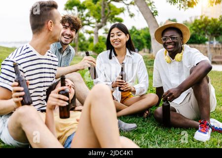 Junge Gruppe von verschiedenen besten Freunden, die sich im Stadtpark beim Biertrinken aufmachen Stockfoto