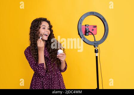 Erstauntes Kind mit langen lockigen Haaren macht Video für Blog halten Puderbürste Stockfoto