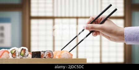 Frau, die Sushi mit Essstäbchen abholt, hat im japanischen Restaurant zu Mittag gegessen Stockfoto
