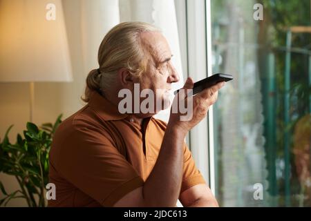 Porträt eines älteren Mannes mit Pferdeschwanz, der Sprachnachrichten auf dem Smartphone aufzeichnet Stockfoto