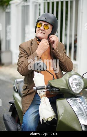 Älterer Mann mit gelber Sonnenbrille und Schutzhelm, wenn er auf dem Roller in der Stadt unterwegs ist Stockfoto