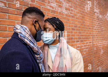 Paar tragen Gesichtsmasken, die sich an einer Ziegelwand gegenüberstehen Stockfoto