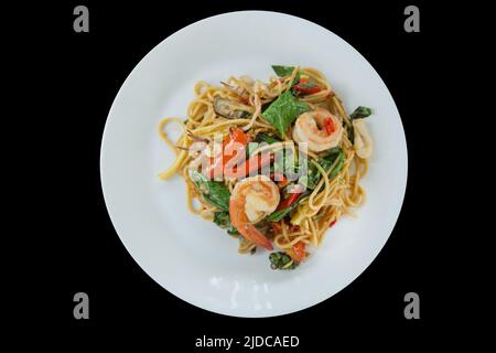 Gestanzte Hand mit Gabel und Spaghetti mit würziger Garnele und Tintenfisch auf schwarz isoliert. Stockfoto