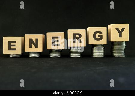 Energiekrise und hohe Preise für Kraftstoff, Öl, Gas und Benzin Konzept. Steigender Stapel von Münzen in Holzblöcken auf dunkelschwarzem Hintergrund. Stockfoto