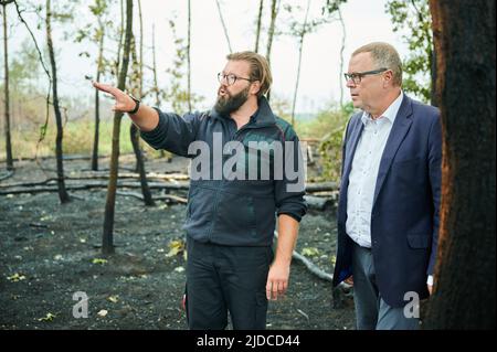 Treuenbrietzen, Deutschland. 20.. Juni 2022. Im verbrannten Waldgebiet in Treuenbrietzen steht der Innenminister des Landes Brandenburg, Michael Stübgen (CDU), während der Leiter der Feuerwehr, Kevin Grigorian, spricht. Inzwischen sind die Brände vollständig gelöscht. Heftige Regenfälle haben den Feuerwehrleuten in der Nähe von Beelitz und bei Treuenbrietzen südwestlich von Berlin geholfen, auszulöschen. Im rund 20 Kilometer entfernten Landkreis Potsdam-Mittelmark waren am Wochenende zwei große Waldflächen verbrannt. Quelle: Annette Riedl/dpa/Alamy Live News Stockfoto