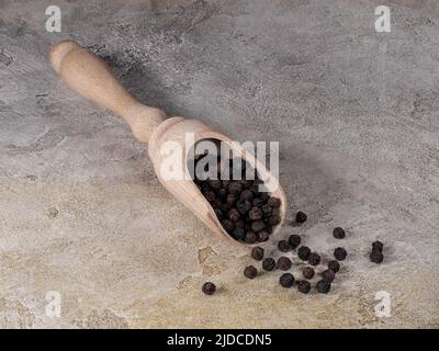 Schwarze Pfefferkörner in Holzschaufel für Gewürze Stockfoto