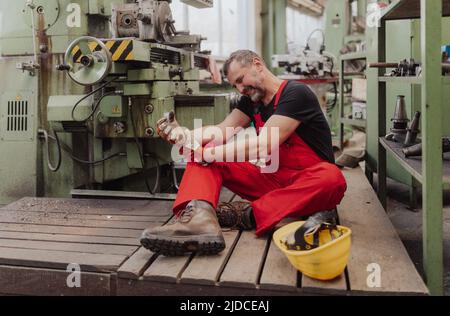 Arbeiter, der nach einem Unfall in der Fabrik unter Schmerzen leidet. Erste-Hilfe-Unterstützung beim Arbeitsplatzkonzept. Stockfoto