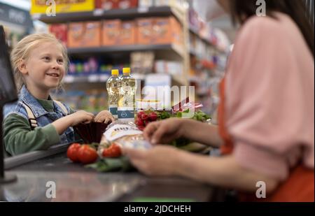 Nahaufnahme eines kleinen blonden Mädchens, das für den Einkauf im Supermarkt bezahlt. Stockfoto